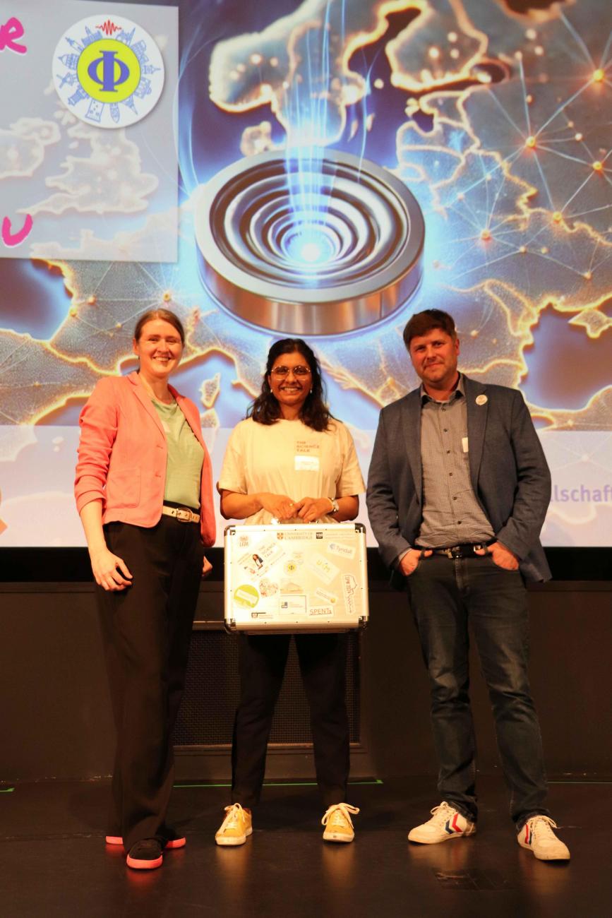 Three people holding a silver suitcase with stickers